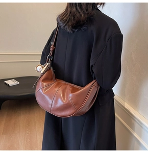 Detail of a brown crescent bag with decorative stitching and baseball bat keychain