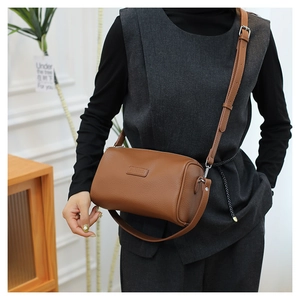 Brown cylinder bag with pebbled leather texture and adjustable strap worn by model