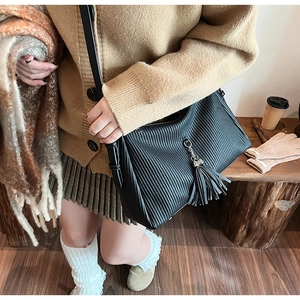 Detail of black pleated tote bag showing vertical texture and elegant leather tassel with chain