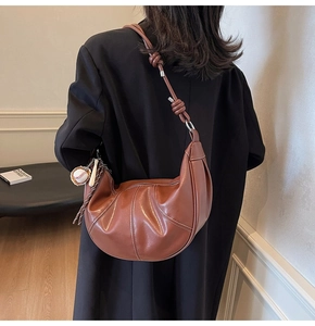 Close-up of brown PU leather crescent bag with stitching details and baseball charm