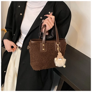 Detail of a brown plush bucket bag with leather handles and a cute teddy bear charm