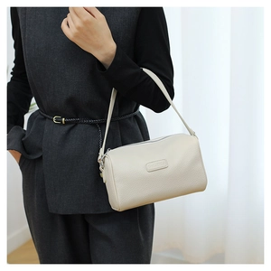 Close-up of a beige pebble leather cylinder bag with silver zipper and logo detail