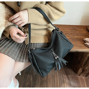 Detail of black pleated PU leather bag with tassel charm and zip closure on wooden bench