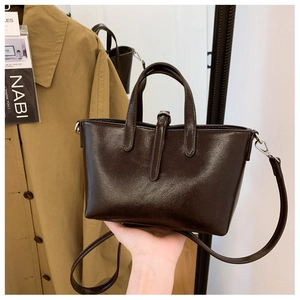 Détail du sac seau en cuir marron foncé brillant avec poignées et bandoulière fine