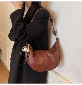 Detail of caramel hobo bag with white stitching and baseball charm on shoulder