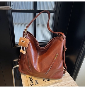 Detailed close-up of brown faux leather tote bag featuring metal zippers and bear charm