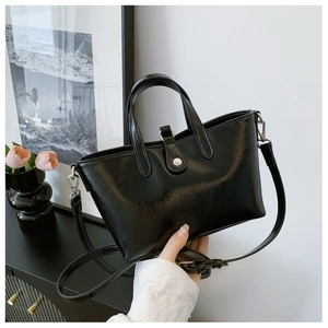 Gros plan sur un sac seau en cuir noir brillant avec doubles poignées et bandoulière