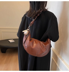 Detailed close-up of brown croissant bag with visible stitching and baseball charm