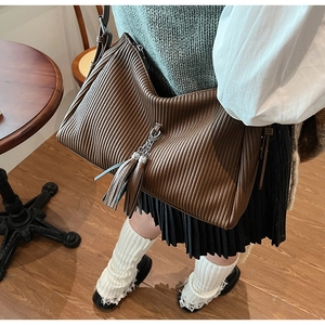 Detail of brown pleated hobo bag featuring vertical texture and dual tassel metal charms