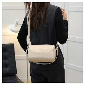 Detailed texture of cream-colored barrel bag with grainy leather and slim shoulder strap