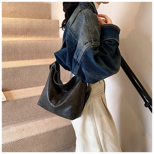 Detail of a vintage black oil wax leather crescent bag worn with a denim jacket