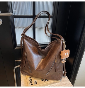 Detail of dark brown vintage tote bag featuring decorative zippers and a plush bear charm