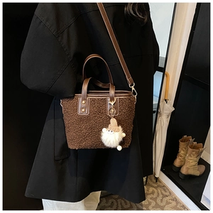 Detail of a brown fuzzy bucket bag with white pompom charm styled on a black coat