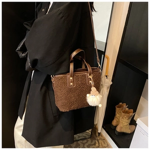 Detail of a brown plush tote bag with leather handles and a cute fuzzy charm