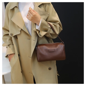 Detail of dark brown cylindrical leather bag with oval embossed logo on trench coat