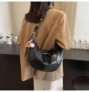 Detail of black croissant bag featuring contrast white stitching and knot strap