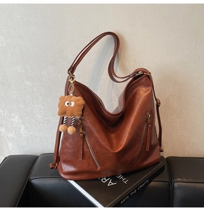Detail of dark brown leather tote bag with zip pockets and plush monster charm