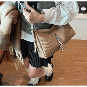 Close-up of khaki pleated leather shoulder bag with stylish fringe tassel and metal buckle