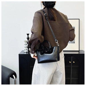 Détail d'un sac seau en cuir noir brillant avec garnitures argentées et bandoulière