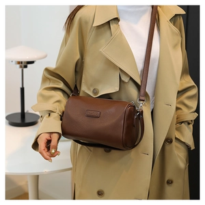 Detail of a dark brown leather cylindrical crossbody bag with pebble texture and adjustable strap