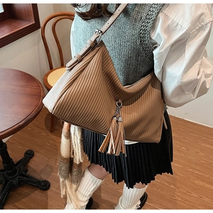Brown hobo bag with vertical pleated texture and leather tassel detail shown on shoulder