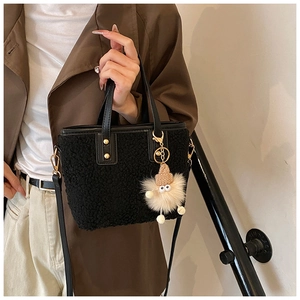 Detail of black fuzzy bucket bag with leather handles and cute plush charm on model
