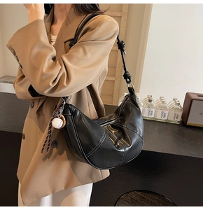 Detail of black leather crescent crossbody bag with white stitching and baseball charm