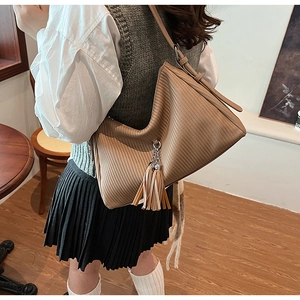 Close-up of brown textured crossbody bag with decorative tassel on a shoulder strap