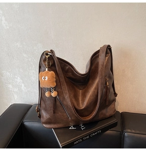 Detail view of large brown retro leather tote with metal zipper and plush charm