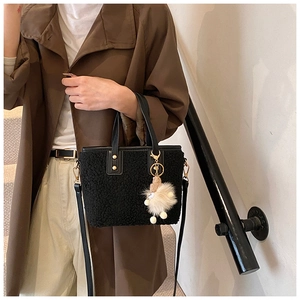 Detail of black faux shearling bucket bag featuring a plush doll charm and leather strap