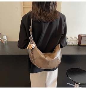Detail of dark brown crescent crossbody bag with baseball charm on a female model