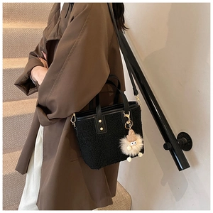 Close-up of black fuzzy bucket bag with leather strap and cute monster plush charm