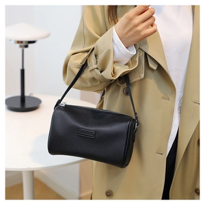 Detail of black pebbled leather cylinder bag with silver metal zipper and thin shoulder strap