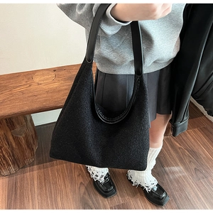 Side view of large black wool tote bag with leather strap worn by a model