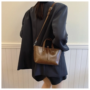Détail d'un sac seau en cuir marron vintage avec garnitures argentées porté sur un blazer