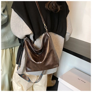 Detail of dark brown leather hobo bag featuring vintage patterned wide shoulder strap