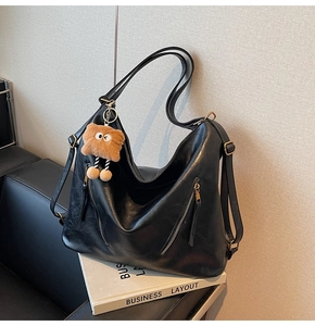 Close-up of black leather tote bag featuring decorative zippers and a cute brown monster charm