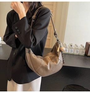 Brown leather hobo bag featuring decorative stitching and baseball charm on shoulder