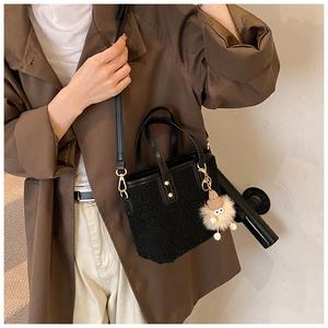 Detail of black faux shearling bucket bag with leather strap on trench coat model