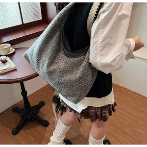 Grey wool hobo bag detail showing the tweed texture and black leather trim in a cafe