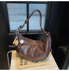 Detail of a brown leather crescent bag with white stitching and baseball charms on books