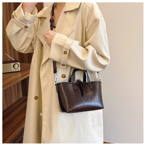 Détail d'un sac seau vintage en cuir marron foncé porté avec un trench-coat beige classique