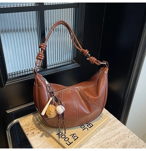 Close-up of brown leather crescent bag with white stitching and baseball charm