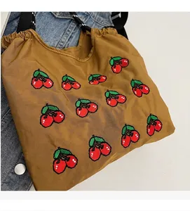 Detail von gestickten Kirschmustern auf einer braunen Canvas-Tasche mit Raffung