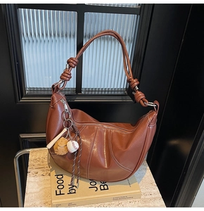 Detail of a dark brown hobo bag with contrast stitching and baseball bag charm accessories