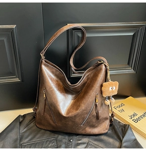 Detail of dark brown vintage faux leather tote with diagonal zippers and plush pendant
