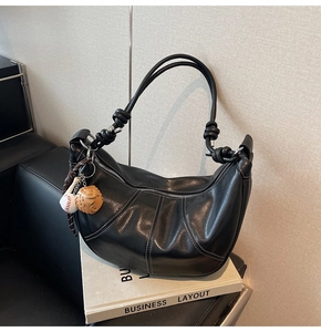 Detail of black leather crescent bag with decorative knot strap and baseball pendant