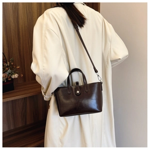 Détail d'un sac seau en cuir marron foncé brillant avec boucle en métal sur manteau