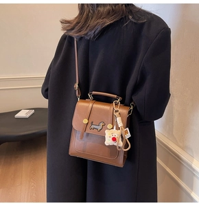 Brown leather crossbody bag with dachshund embroidery and plush charm worn on black coat