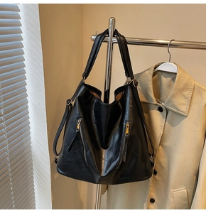 Detail view of a large black soft leather tote bag with gold zippers hanging on a hanger